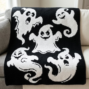 May include: A black and white crochet blanket featuring a pattern of five distinct ghosts with various facial expressions. The ghosts are arranged across the rectangular textile, showcasing detailed white yarn stitches against a solid black background.