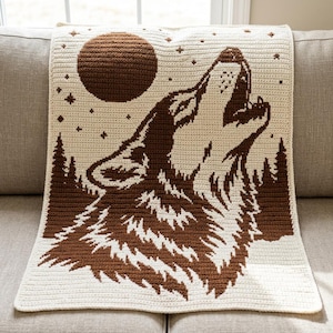 Può includere: Una coperta rettangolare all'uncinetto con un design bicolore marrone e crema. Il motivo raffigura un lupo che ulula a una grande luna circolare, circondato da una foresta di pini e piccole forme di stelle su uno sfondo color crema.