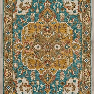 May include: Rectangular area rug with an ornate, traditional design. The rug features a central medallion in shades of gold, teal, and rust, surrounded by a teal field and a border of olive green and cream. The rug is placed on a light wood floor.