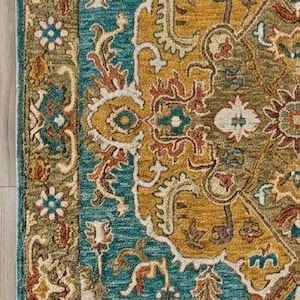 May include: Close-up of a decorative area rug with an intricate floral pattern. The rug features a teal, gold, and cream color palette with a detailed border. The rug's design includes stylized flowers and leaves, creating a classic, elegant look.