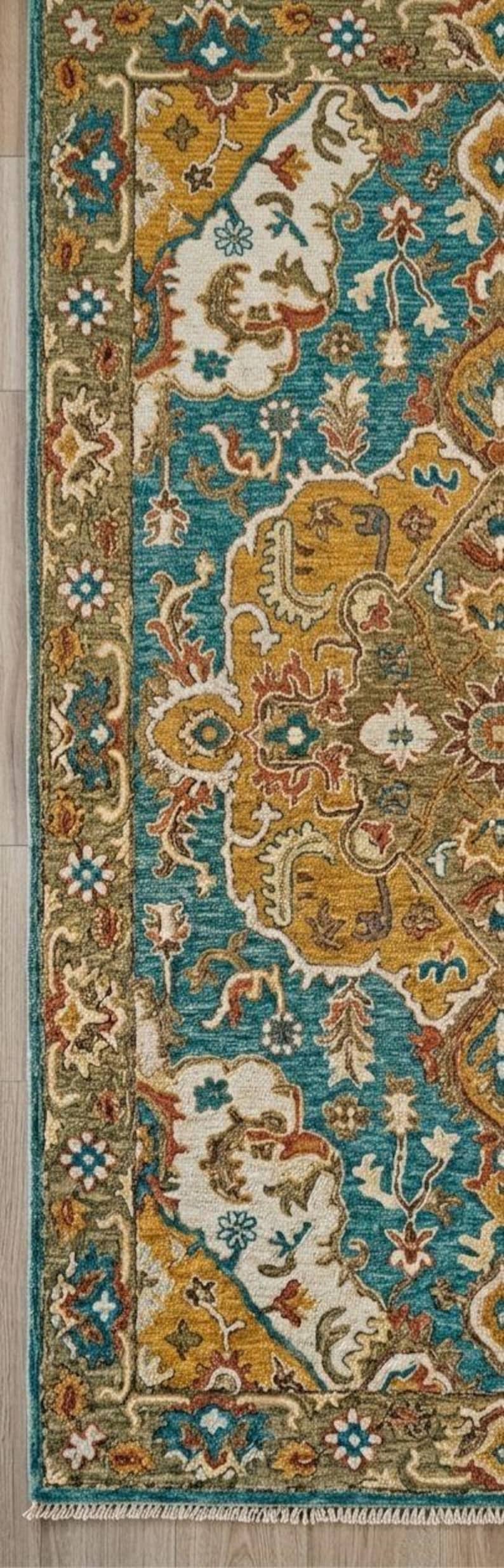 May include: Close-up of a decorative area rug with an intricate floral pattern. The rug features a teal, gold, and cream color palette with a detailed border. The rug's design includes stylized flowers and leaves, creating a classic, elegant look.