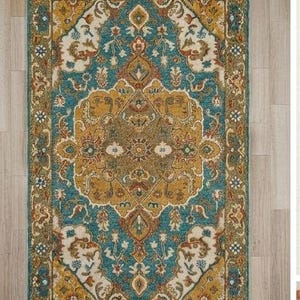 May include: A rectangular area rug with an ornate, traditional design. The rug features a central medallion in shades of gold and brown, surrounded by a teal background and a border with floral and geometric patterns. The rug has a fringed edge.