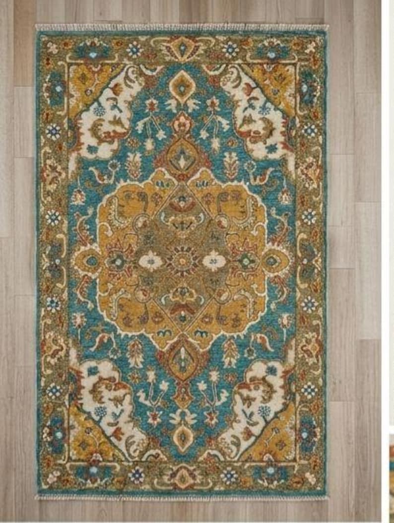 May include: A rectangular area rug with an ornate, traditional design. The rug features a central medallion in shades of gold and brown, surrounded by a teal background and a border with floral and geometric patterns. The rug has a fringed edge.