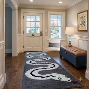 Puede incluir: Una alfombra pasillera rectangular de color gris con un gran diseño de serpiente blanca serpenteante, detalles en negro, ojos verdes y lengua roja. La alfombra está sobre un suelo de madera oscura en un pasillo con puerta blanca y banco.