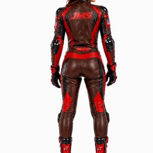 May include: A brown, black, and red leather motorcycle racing suit featuring the text JMS in red on the back. The suit includes integrated protective armor on the shoulders, elbows, and knees, along with small American flag patches on the sleeves.