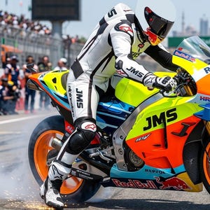 May include: A motorcycle racer in a white and black Alpinestars leather suit and white helmet riding a bright yellow, orange, and blue racing motorcycle. The bike features JMS and Red Bull branding, with sparks flying from the rear tire.