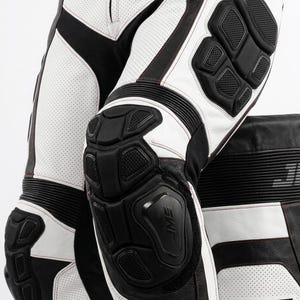 May include: White and black leather motorcycle pants featuring perforated panels, black protective knee and hip armor, accordion stretch zones above the knees, and the text JMS printed in black on the lower leg section of the garment.