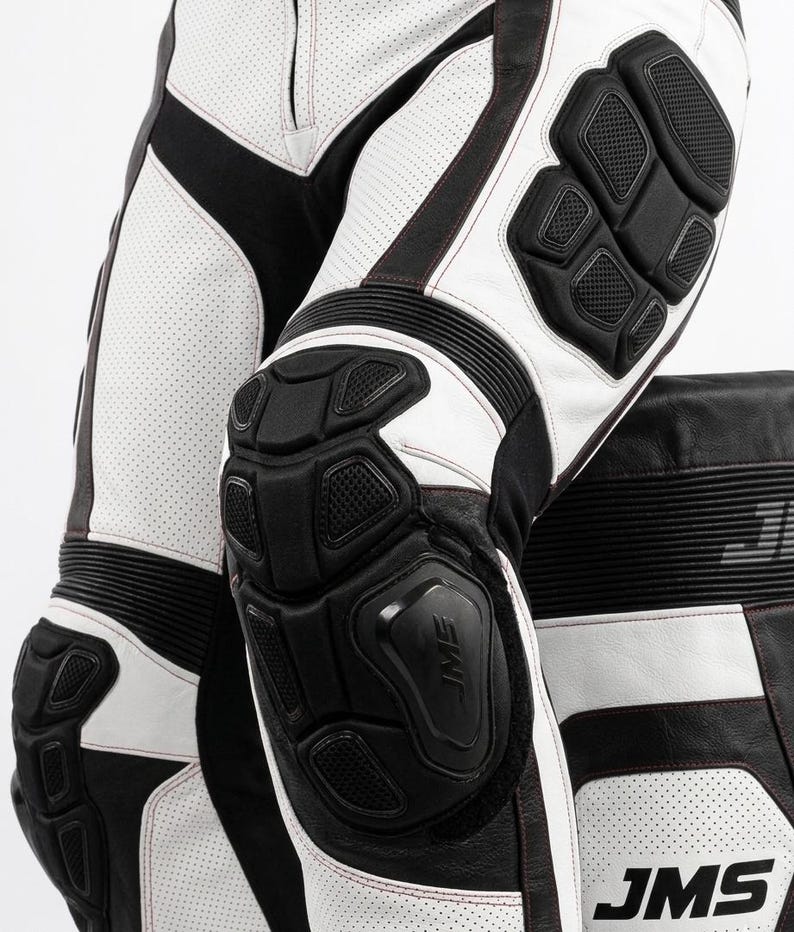 May include: White and black leather motorcycle pants featuring perforated panels, black protective knee and hip armor, accordion stretch zones above the knees, and the text JMS printed in black on the lower leg section of the garment.