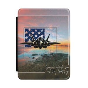 Pode incluir: Uma capa de telefone retangular com uma silhueta de jato preto sobre um design de bandeira americana. O fundo mostra um pôr do sol sobre o mar. O texto "Sunrise over the sea makes my heart sing" está escrito na parte inferior.