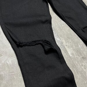 Op de afbeelding: Close-up van een zwarte denim jeans met distressed details. De jeans heeft gescheurde secties bij de knie&euml;n. De stof lijkt een medium-gewicht denim te zijn. Klassiek vijf-zakken ontwerp.