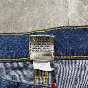 May include: Close-up of a blue denim garment with a tag. The tag displays care instructions and fabric content: 100% cotton. The tag also includes the style number MDE859R66 and RN#112790.