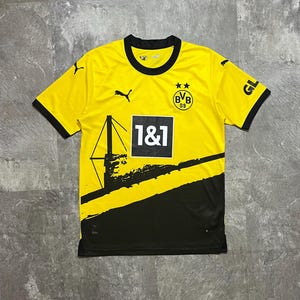 May include: A yellow and black soccer jersey with the BVB 09 logo and the 1&1 logo. The jersey has black trim on the collar and sleeves. The Puma logo is visible on the chest and sleeves.