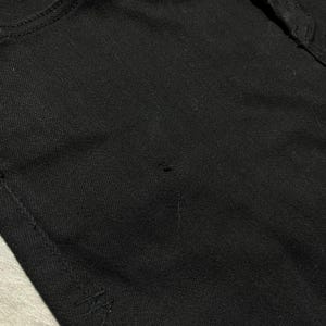 Op de afbeelding: Close-up van een zwarte spijkerbroek. De jeans heeft een klassiek ontwerp met vijf zakken, met een zichtbare voorzak en een klein logodetail aan de onderkant. De stof lijkt een stevige, donker gewassen denim te zijn.