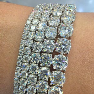 May include: Close-up of several diamond tennis bracelets. The bracelets feature round and square-cut diamonds set in a silver metal. The diamonds sparkle and reflect light, creating a brilliant display of luxury and elegance. The bracelets are stacked together.