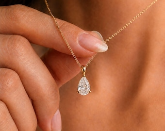 May include: A gold chain necklace featuring a single pear-shaped clear gemstone pendant. The pendant is held by a gold setting and hangs from a delicate gold link chain. The clear stone has a faceted surface that reflects light, creating a bright appearance.