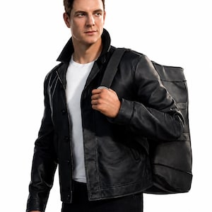 May include: A black leather jacket with a pointed collar, long sleeves, and a front button closure, worn over a plain white t-shirt. A large black rectangular bag with horizontal stitched detailing is carried over the shoulder by a wide strap.