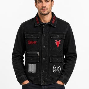 Puede incluir: Chaqueta vaquera negra con detalles bordados en rojo. Incluye el nombre de la banda "Slipknot", una cabeza de cabra roja y el texto "stone deff*". Incluye múltiples bolsillos y un código de barras.