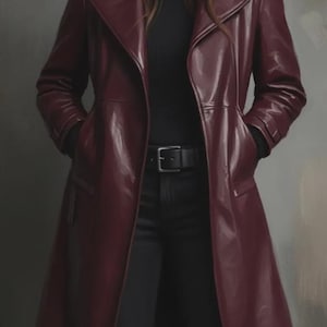 Puede incluir: Un abrigo largo de cuero burdeos con un acabado brillante. El abrigo presenta un cuello con solapas clásico, un cinturón en la cintura y bolsillos. La persona lleva un cuello alto negro y pantalones negros.