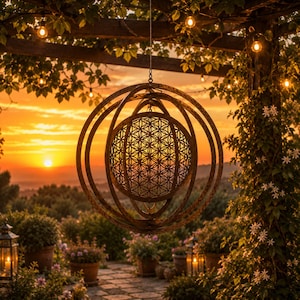 May include: A hanging metal sphere sculpture featuring an intricate laser-cut flower of life geometric pattern within concentric rings. The bronze-toned object is suspended by a thin wire, showcasing a detailed circular lattice design.