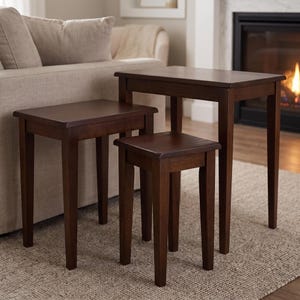 May include: A set of three dark brown wooden nesting tables with rectangular tops and four straight legs each. The tables are arranged in a tiered formation, with the largest table in the back, the medium in the middle, and the smallest in front.