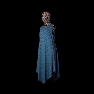 May include: A sleeveless teal dress featuring a dark blue diamond-shaped geometric pattern throughout. The garment has a round neckline and an asymmetrical hemline that falls longer on one side, displayed on a wire-frame mannequin head and torso.