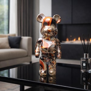 Op de afbeelding: Decoratief berenbeeldje met een uniek patroon van oranje, bruine en witte wervelingen. De beer staat op een zwarte tafel en reflecteert het licht. Het beeldje heeft een glanzende afwerking en is een modern kunstwerk.