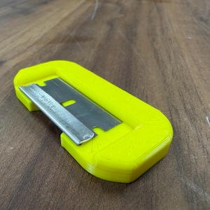 May include: A bright yellow utility knife with a silver blade. The blade is partially inserted into the yellow plastic housing. The knife is designed for cutting tasks.