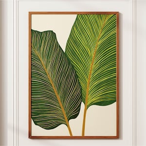 Puede incluir: Una pieza de arte mural rectangular que muestra dos grandes hojas tropicales superpuestas en tonos verde oscuro y verde amarillento con venas claras prominentes. La obra está enmarcada en un marco de madera de tono medio.