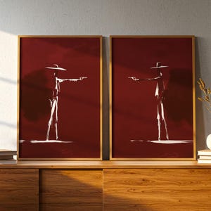 Pode incluir: Dois quadros de parede com fundo vermelho profundo e a silhueta branca de uma figura com um chapéu de abas largas segurando uma pistola. Cada impressão está emoldurada numa moldura dourada fina, exibindo uma representação artística.