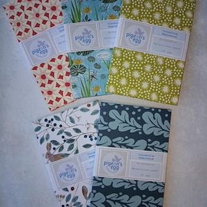 May include: A selection of concertina sketchbooks with patterned covers. Designs include floral, botanical, and nature-inspired motifs in red, green, blue, and white. Each sketchbook has a label that reads "pigeon's egg" and "Bockingford Watercolour paper 190 gsm."