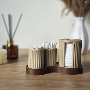 May include: A beige and brown bathroom organiser with three compartments. The organiser holds cotton swabs and cotton pads. A candle, diffuser, and vase are in the background.