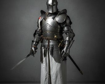 以下が含まれることがあります： 磨き上げられた鋼鉄製のプレートアーマー一式。閉じたヘルメット、関節付きの肩当て、ガントレット、胸当てが特徴です。金属製の鎧の下には長い白い布製のチュニックを着用しており、右手には鋼鉄製の剣を握っています。