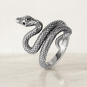 Peut inclure: Une bague en métal argenté en forme de serpent enroulé. La bague présente des écailles texturées détaillées couvrant tout le corps du serpent, avec une tête et des yeux définis. Le design s'enroule pour former une structure de bande ouverte.