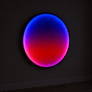 May include: A circular wall light fixture featuring a smooth gradient of vibrant colors. The top portion of the circle glows in a deep blue, transitioning through a soft violet into a bright, saturated red at the bottom edge, encased in a thin frame.