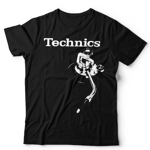 May include: A black short-sleeved t-shirt featuring a white graphic print of a turntable tonearm and the word Technics in a bold serif font. The design is positioned on the upper chest area of the shirt, showcasing a high-contrast visual.
