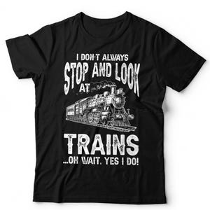 May include: A black short-sleeved t-shirt featuring a white graphic of a steam locomotive train. The text reads: I DON'T ALWAYS STOP AND LOOK AT TRAINS...OH WAIT, YES I DO! The design is centred on the chest with a distressed, vintage-style font.