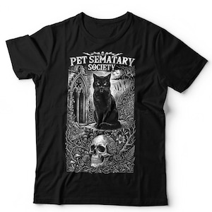 May include: A black t-shirt featuring a white graphic print of a black cat sitting on a stone structure in front of a gothic archway. Below the cat is a human skull surrounded by roses and vines. The text PET SEMATARY SOCIETY is printed above.