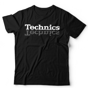 May include: A black short-sleeved t-shirt featuring the word Technics printed in white on the chest. Below the main text, a mirrored, horizontally striped version of the same word is displayed in a lighter, faded grey tone.