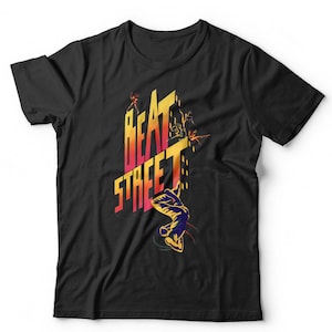 May include: A black short-sleeved t-shirt featuring a graphic print on the chest. The design displays the text BEAT STREET in a yellow-to-red gradient font, accompanied by silhouettes of figures in dynamic poses and city building outlines.