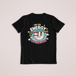 May include: A black t-shirt featuring a graphic of a sloth hanging from a tree branch. The text reads I'M ON ENERGY SAVING MODE in yellow and pink letters. The design includes small white clouds, green leaves, and a crescent moon around the sloth.