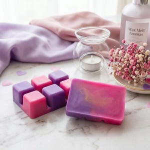 Puede incluir: Imagen con temática de aromaterapia con ceras perfumadas rosas y moradas, una vela y un difusor. La imagen incluye una botella de "Wax Melt Aromas" y un pequeño ramo de flores rosas. Las ceras perfumadas están en un soporte.