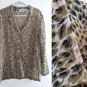 Puede incluir: Una camisa de manga larga con botones y estampado de leopardo en tonos marrones, negros y blancos. La camisa está hecha de una tela fina y sedosa.