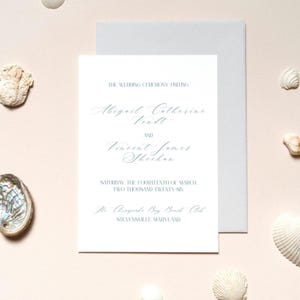 以下が含まれることがあります： エレガントな筆記体の結婚式の招待状。招待状には、Abigail Catherine Vendl と Vincent James Sheehan の名前、日付、会場であるメリーランド州スティーブンスビルの The Chesapeake Bay Beach Club が記載されています。招待状は白で、水色の封筒が付いています。