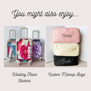 May include: Three miniature clear rolling suitcases with retractable handles, two labeled with the names Caroline and Abigail, alongside a stack of three rectangular zippered pouches in pink, cream, and black, labeled with the names Emilia and Carter.