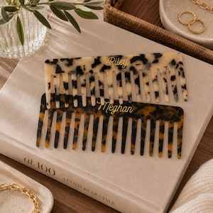 May include: Two rectangular hair combs with a tortoiseshell pattern. The top comb is cream and brown with the name Riley in gold script. The bottom comb is dark brown and amber with the name Meghan in gold script. Both combs feature wide teeth.