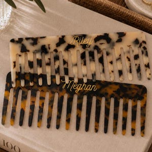 May include: Two wide-tooth hair combs with a tortoiseshell pattern. The top comb is cream and brown with the name Riley printed in gold script. The bottom comb is dark brown and amber with the name Meghan printed in gold script.