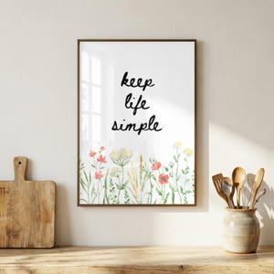 May include: A framed art print with the words "keep life simple" in black script. The bottom of the print features a watercolor illustration of wildflowers in shades of red, yellow, and green. The frame is a dark brown color.