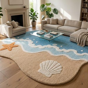 May include: An irregularly shaped area rug featuring a beach-themed design with a sandy beige shore, light blue ocean water, and white foam waves. The rug includes a textured orange starfish and a large white seashell motif on the sand surface.