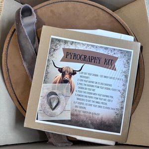 May include: A pyrography kit in a cardboard box. The kit includes a round, brown leather hat, a ribbon, and instructions. The instructions feature a picture of a longhorn and a hat design. The text on the instructions reads "PYROGRAPHY KIT".