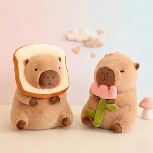 May include: Two plush capybara toys. The left capybara is framed by a slice of white bread with a brown crust. The right capybara holds a pink flower with a green stem. Both have brown snouts, small dark eyes, and soft tan fur.